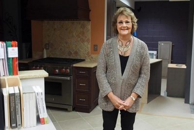 Ellen Cheever stands beside materials in her recently donated collection of publications spanning her career in the kitchen and bath industry. Behind her, still under construction at the time, is the library space that now houses her collection.