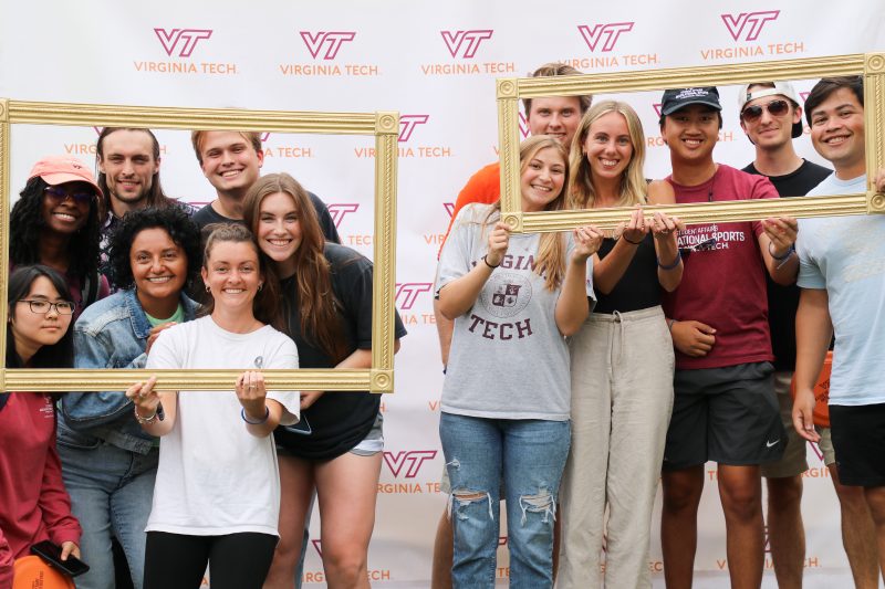 Students smiling together on a Virginia Tech backdrop holding picture frames.
