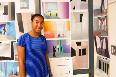 Student standing in front of work pinned up on the wall.