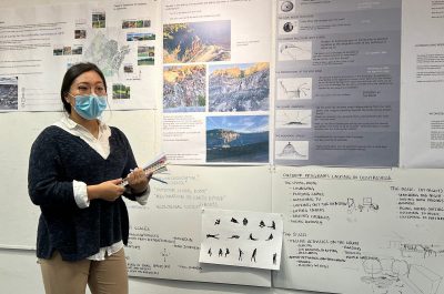 Student standing in front of pin ups presenting work