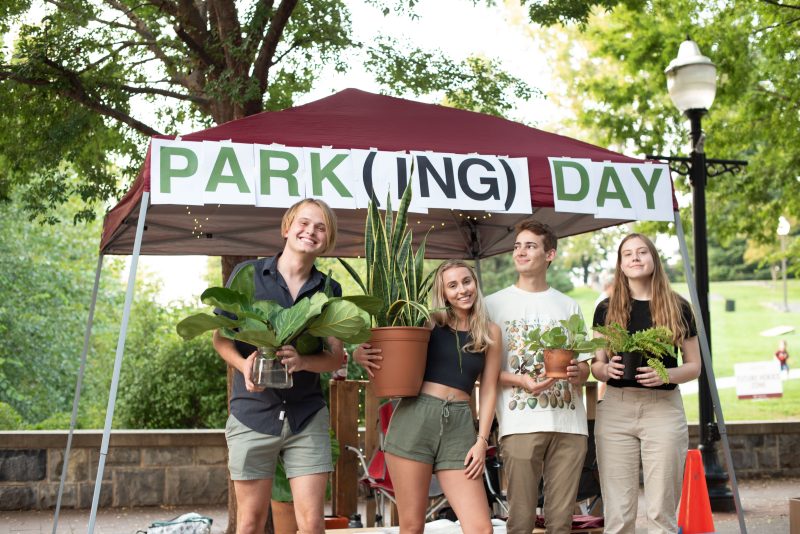 Four students outside holding plants under a tent that says  PARK(ING) DAY