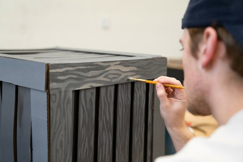 Back of student painting a wooden box.